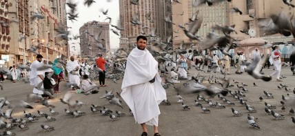 A man in ihram clothes among flying pigeons